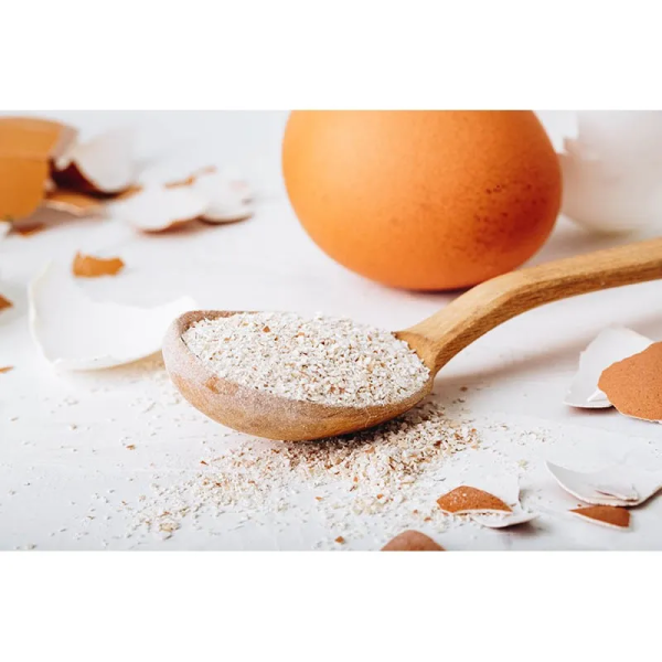 booster de repas pour chat calcium Cooka's Cookies dans une cuillière en bois avec un oeuf et des coquilles d'oeuf à côté